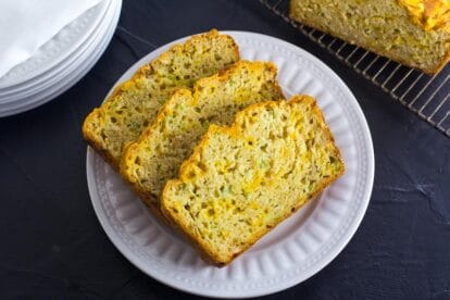 3 thick slices of cheesy beer bread arranged on a decorative white plate resting on a dark surface; cooling rack in background