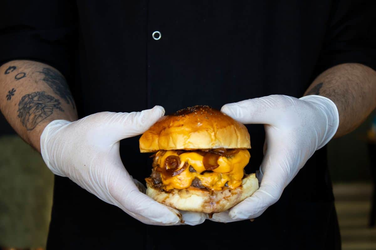 Man in gloves holding cheeseburger.