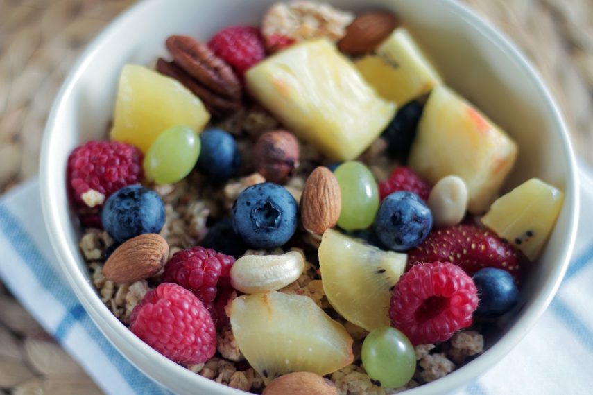 a white bowl with blueberries, grapes, nuts, raspberries and kiwi on top of a white and blue napkin