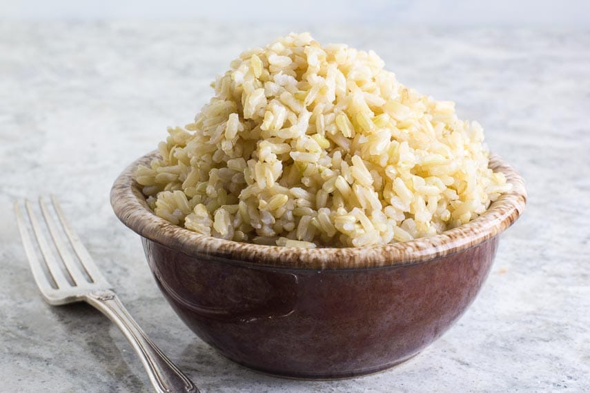 brown rice in a brown ceramic bowl with silver fork