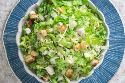chopped chicken Caesar salad in white serving bowl on round blue placemat