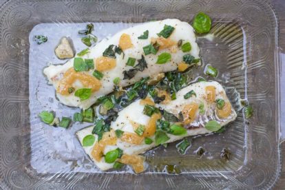 cod with preserved lemons & basil in decorative glass dish on brown surface