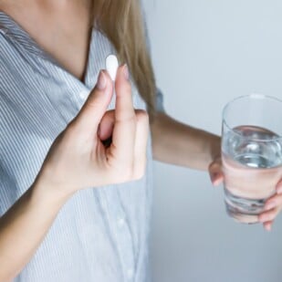 Woman taking a pill with a glass of water.