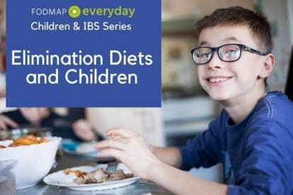 A young boy with a blue shirt and glasses smiling at the camera while he is eating a meal.