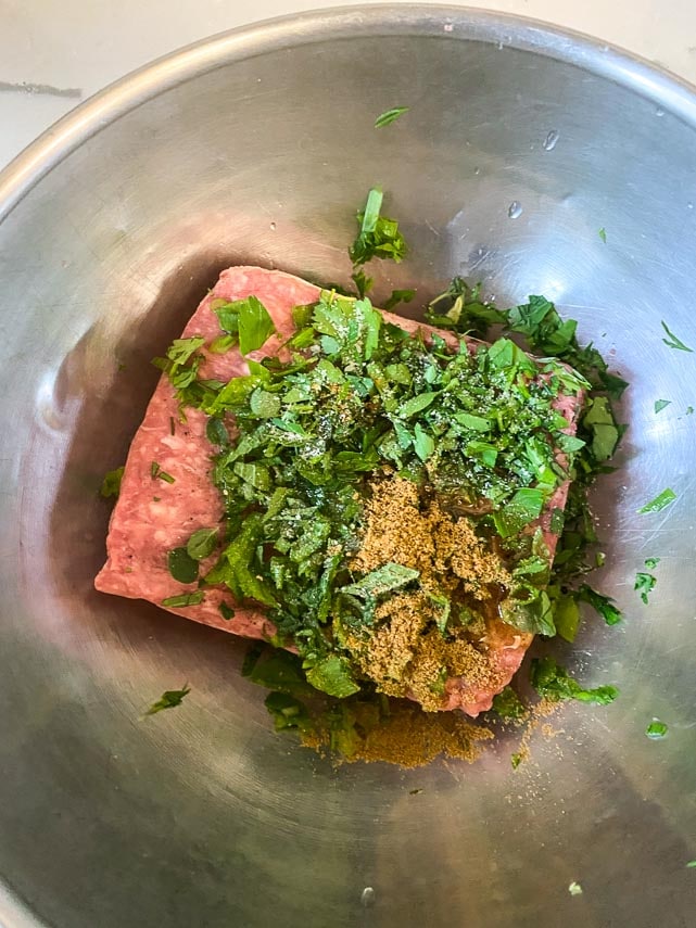 flavoring lamb burgers with cumin and fresh herbs in metal bowl