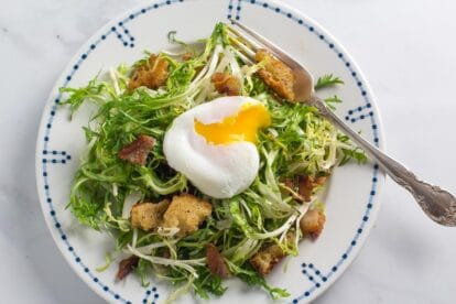 frisée salad with poached egg (broken open) on white plate with blue border