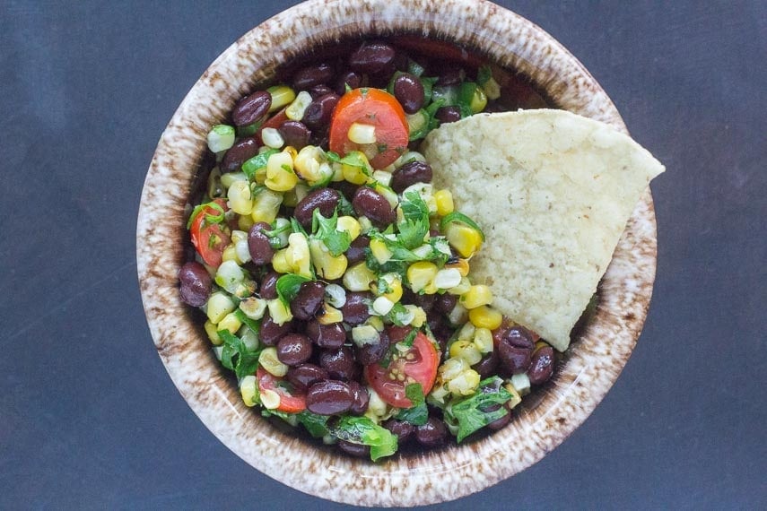 grilled corn salsa with black beans in a small bowl and a corn chip for dipping