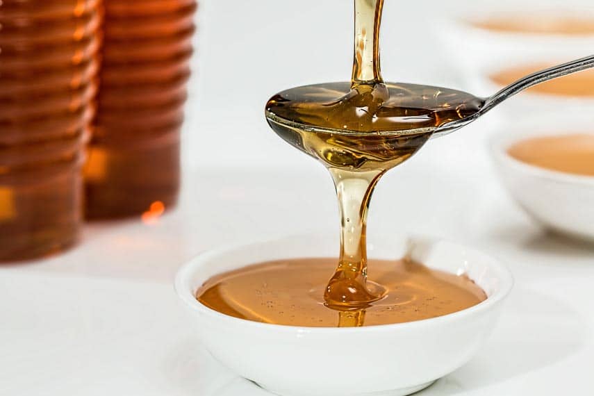 honey pouring into a spoon, overflowing into a white bowl honey pouring into a spoon, overflowing into a white bowl