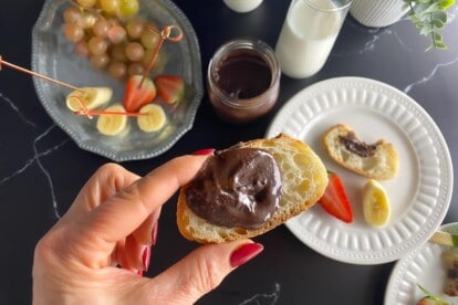 horizontal image on Low FODMAP Nutella on bread held in manicured hand against dark background