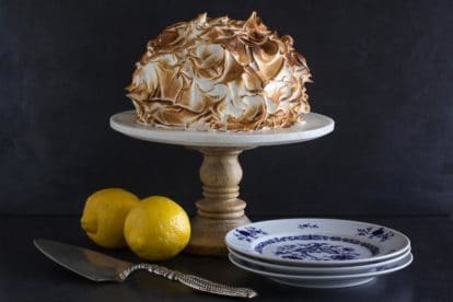 horizontal Low FODMAP lemon meringue cake on white pedestal with dark background