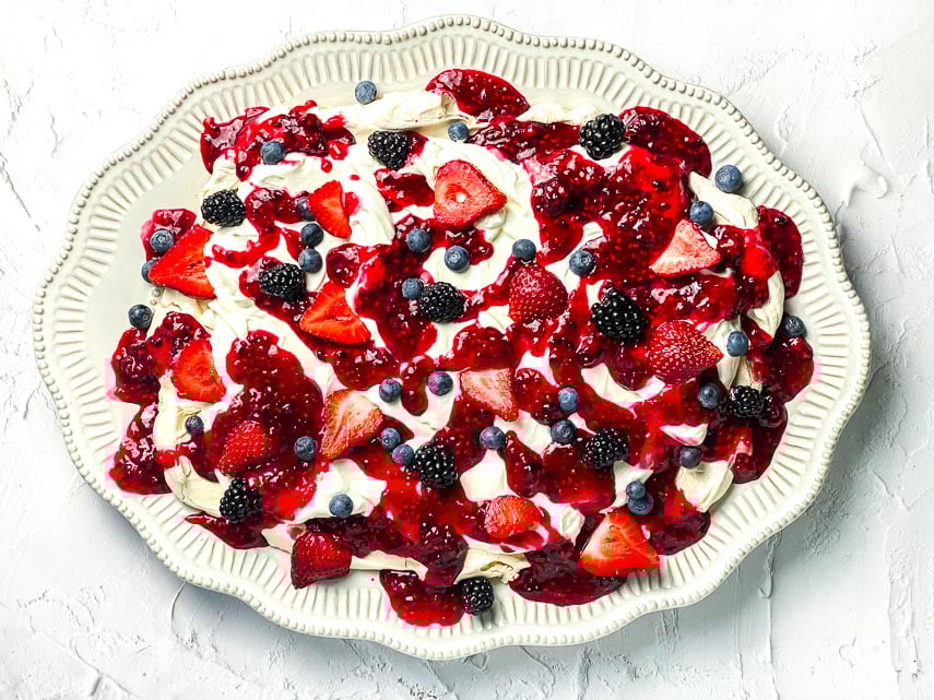 horizontal image of low FODMAP Mixed Berry Slab Pavlova on decorative oval plate; white background