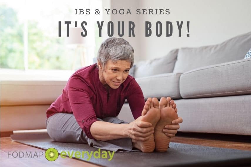A middle aged woman sitting on the floor and stretching forward holding her feet. 