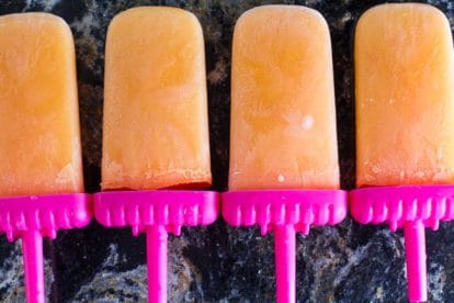icy low FODMAP Cantaloupe lime popsicles on dark quartz surface