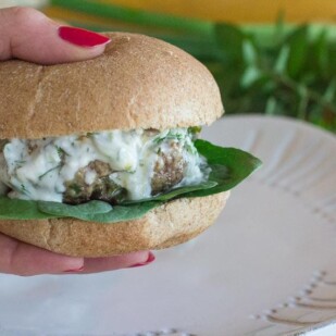 lamb burger with tzatziki sauce, held in hand over a white plate