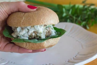 lamb burger with tzatziki sauce, held in hand over a white plate