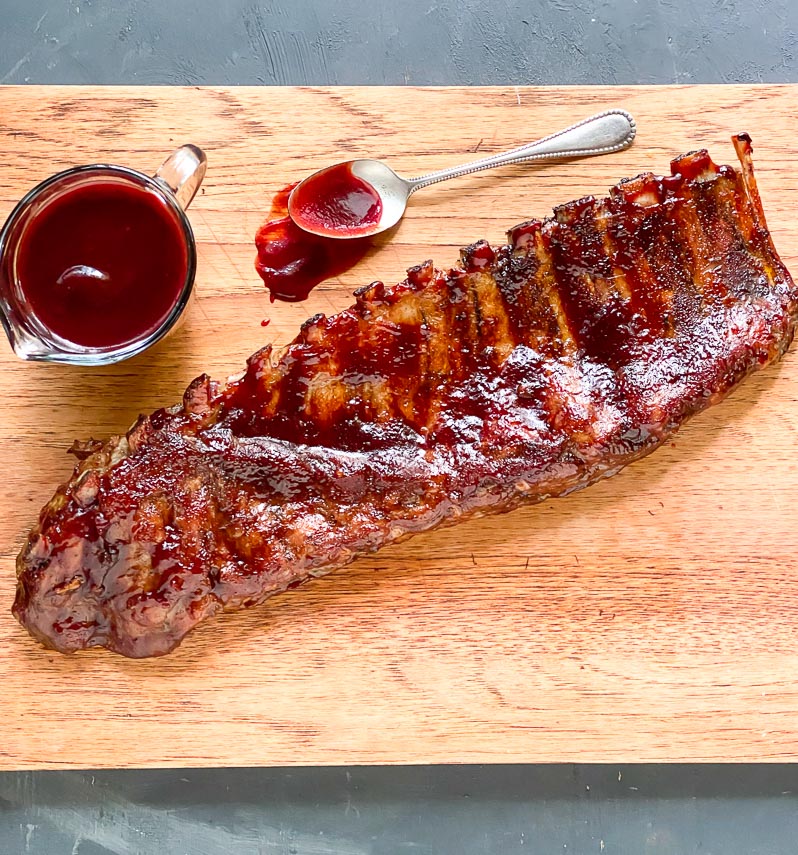 low FODMAP Blackberry Maple BBQ Ribs on wooden board; extra sauce alongside