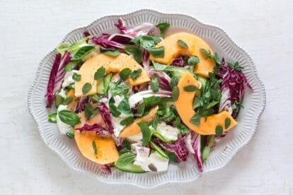 low fodmap cantaloupe, cucumber and burrata salad with herbs on a white platter and white wooden surface