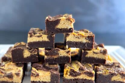 Low FODMAP Pumpkin Cheesecake Brownies stacked on a white plate, dark background