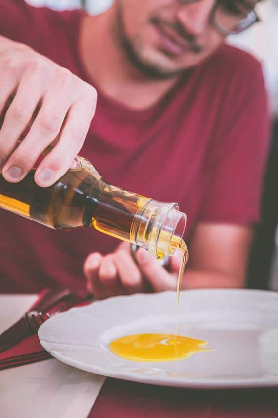 man pouring oil on white plate