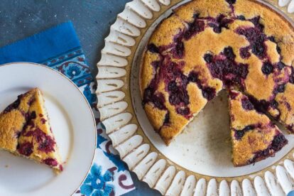 Overhead image of Low FODMAP Cornmeal Berry Snack cake with berries; whole cake with slice out; slice on white plate; blue background