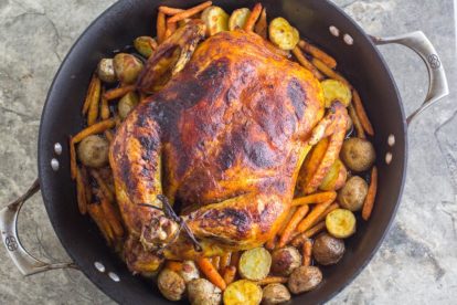 overhead image of whole roasted curry chicken with potatoes and carrots in a roasting pan against a stone backdrop