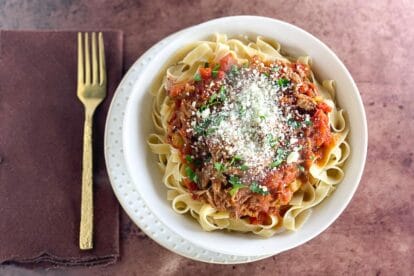 overhead Instant Pot Pork Ragu over noodles in white bowl on brown surface