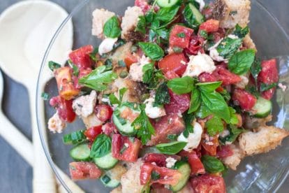 overhead Low FODMAP Panzanella with Tomatoes, Cucumbers & basil in a glass pedestal dish with wooden servers alongside