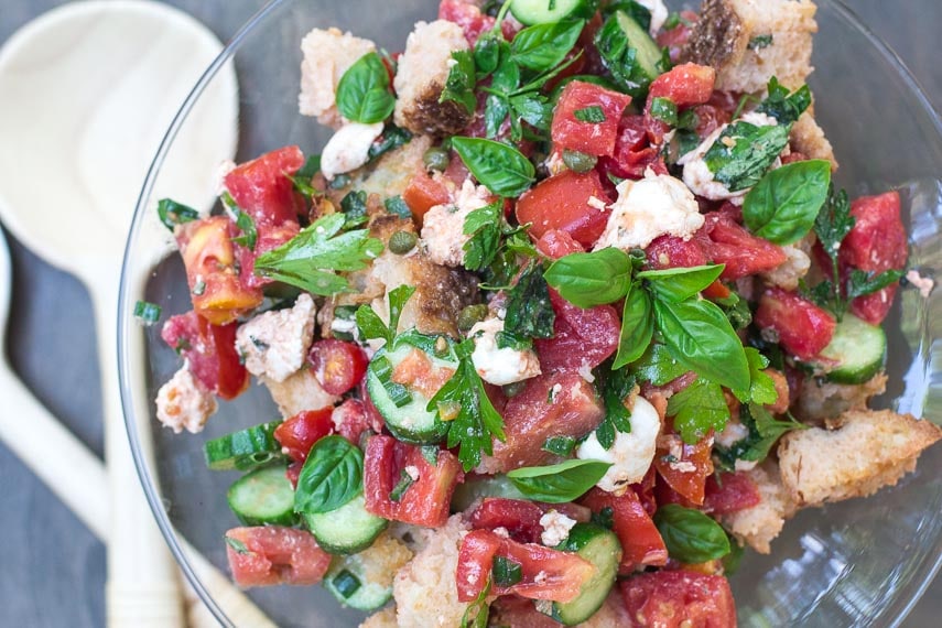 overhead Low FODMAP Panzanella with Tomatoes, Cucumbers & basil in a glass pedestal dish with wooden servers alongside
