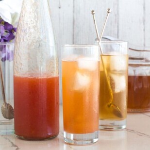 peach iced tea in tall glasses with silver spoons against white backdrop_