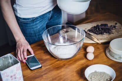 Woman cooking at home. Closeup of woman hands making cookies in kitchen using cellphone to learn recipe.