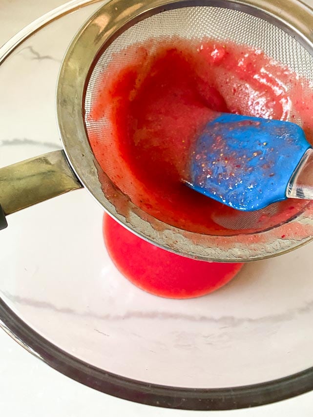 pressing strawberry purée through fine mesh strainer over glass bowl