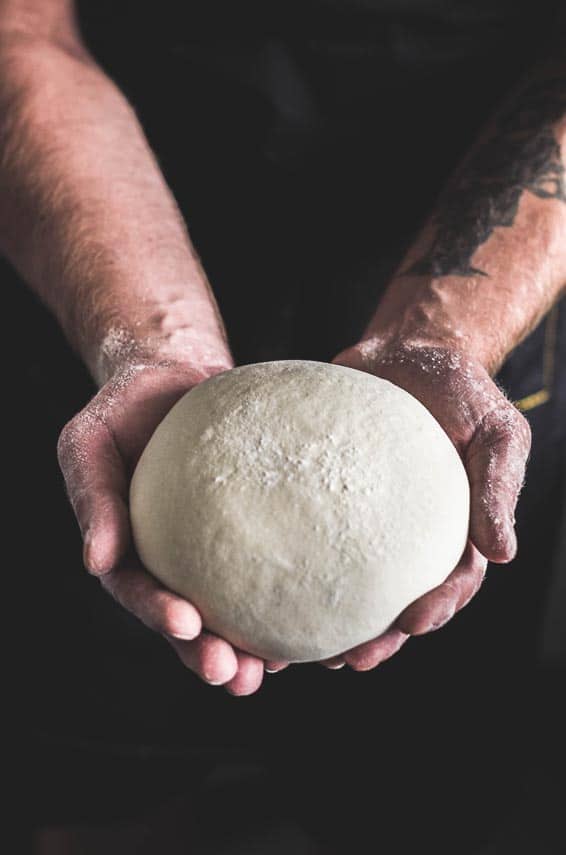 raw bread dough in man's hands; dark background raw bread dough in man's hands; dark background