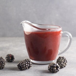 side view of low FODMAP Blackberry Maple BBQ Sauce in clear pitcher, dark table