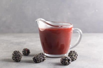 side view of low FODMAP Blackberry Maple BBQ Sauce in clear pitcher, dark table