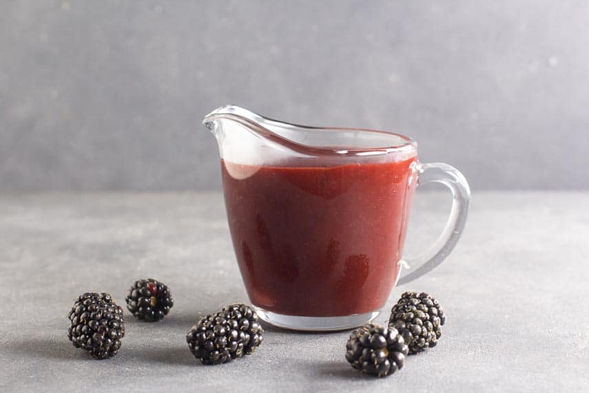 side view of low FODMAP Blackberry Maple BBQ Sauce in clear pitcher, dark table