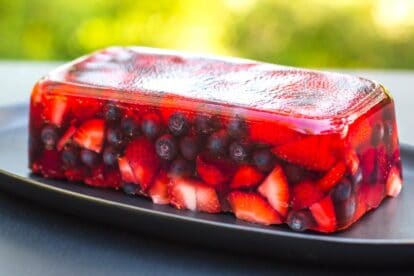 side view of Low FODMAP Mixed Berry Terrine on an oval black plate; outside on deck - garden in background