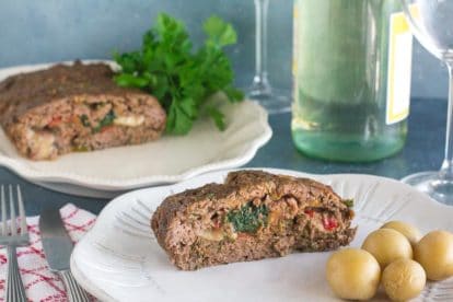 slice of stuffed meatloaf with spinach and provolone on white plate with steamed potatoes