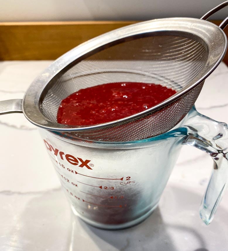 straining blackberry purée into a measuring cup