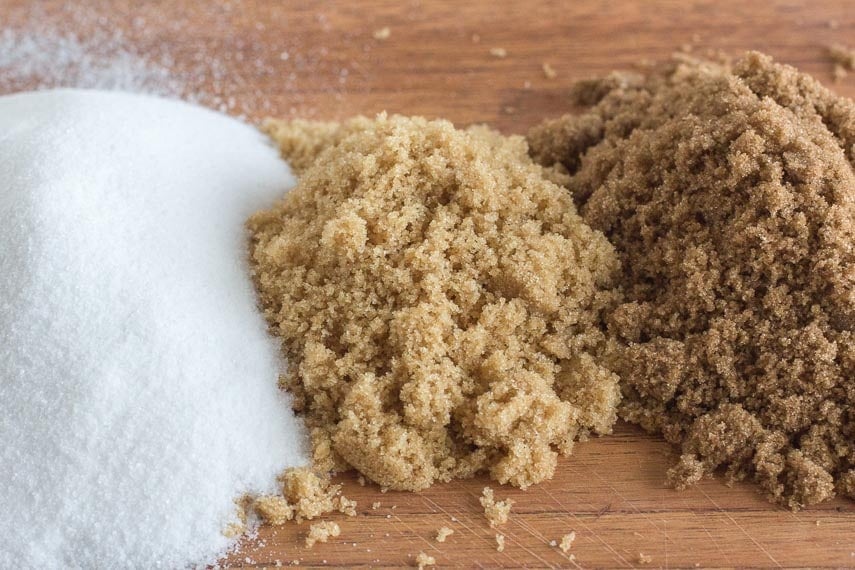 Granulated white sugar, light brown sugar and dark brown sugar on a wooden cutting board