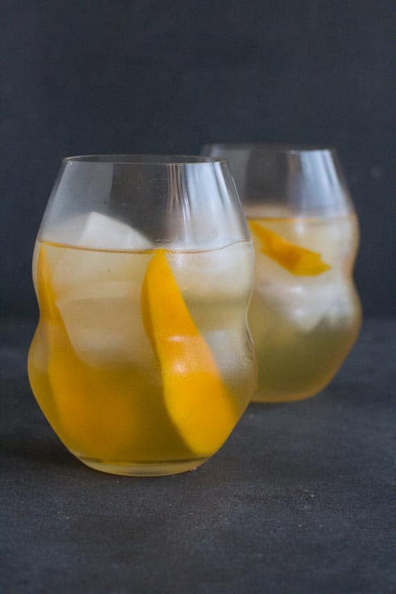 vertical image of low FODMAP Iced White Tea with Mango in decorative clear glasses on dark background