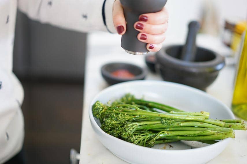 woman preparing broccolini in a white bowl